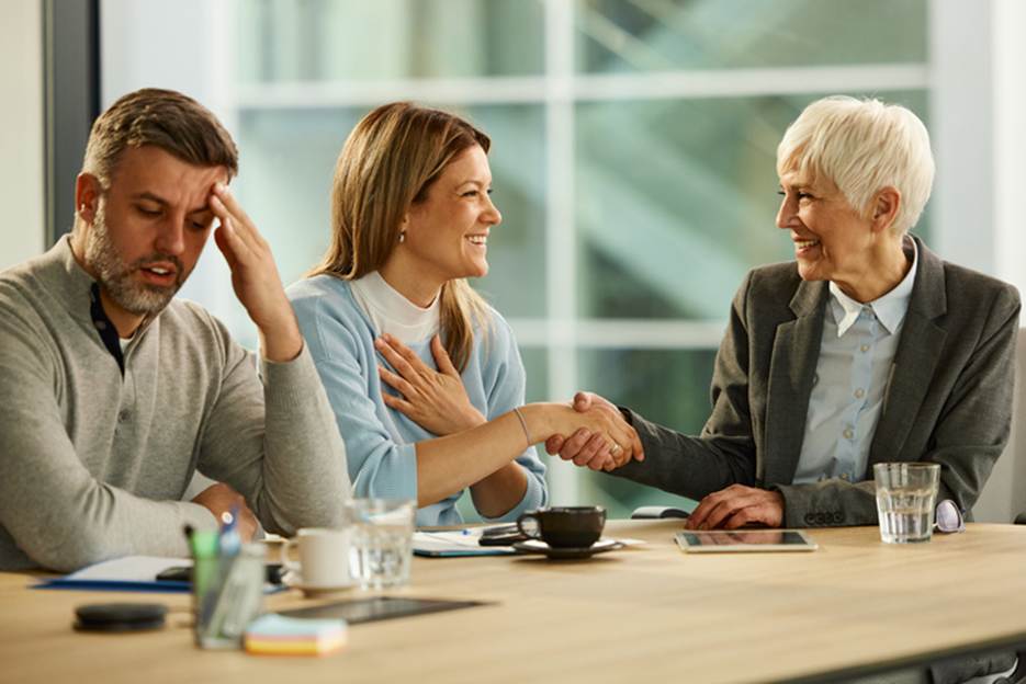 A business deal concludes with a handshake. One participant looks distressed at the meeting's outcome as an editor focuses on "main content."